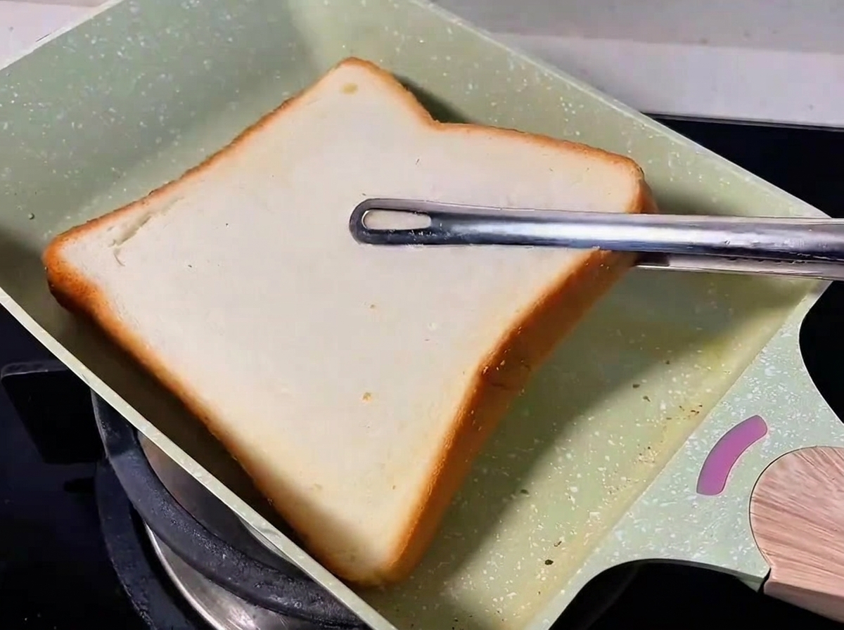 A slice of white bread toasting in a green pan.