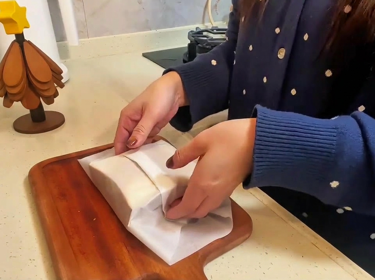The finished beef and cheese sandwich wrapped in parchment paper being sliced in half on a wooden board.