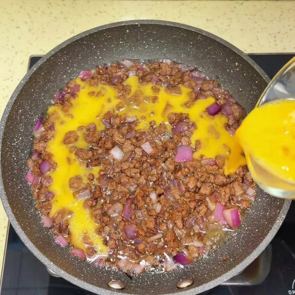 Ground beef being broken down in a hot frying pan with a spatula.