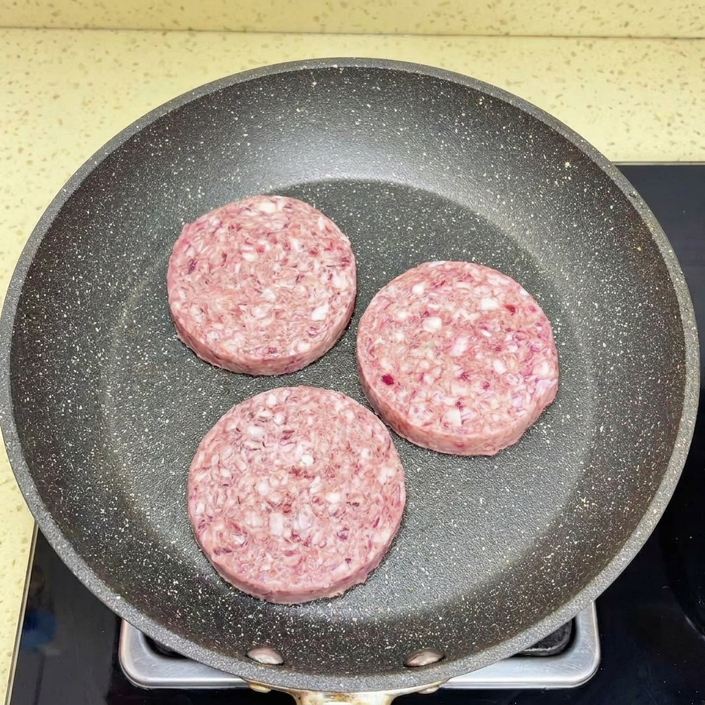 Ground beef being crumbled and broken apart in a hot frying pan using a white spatula.