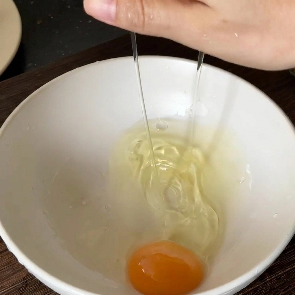 Fresh egg being cracked into a white bowl.