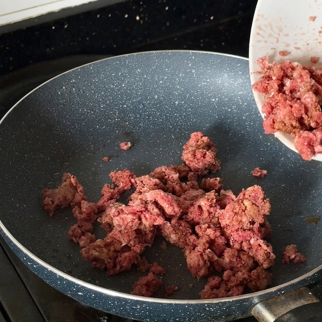 Seasoned minced beef browning in a hot frying pan.