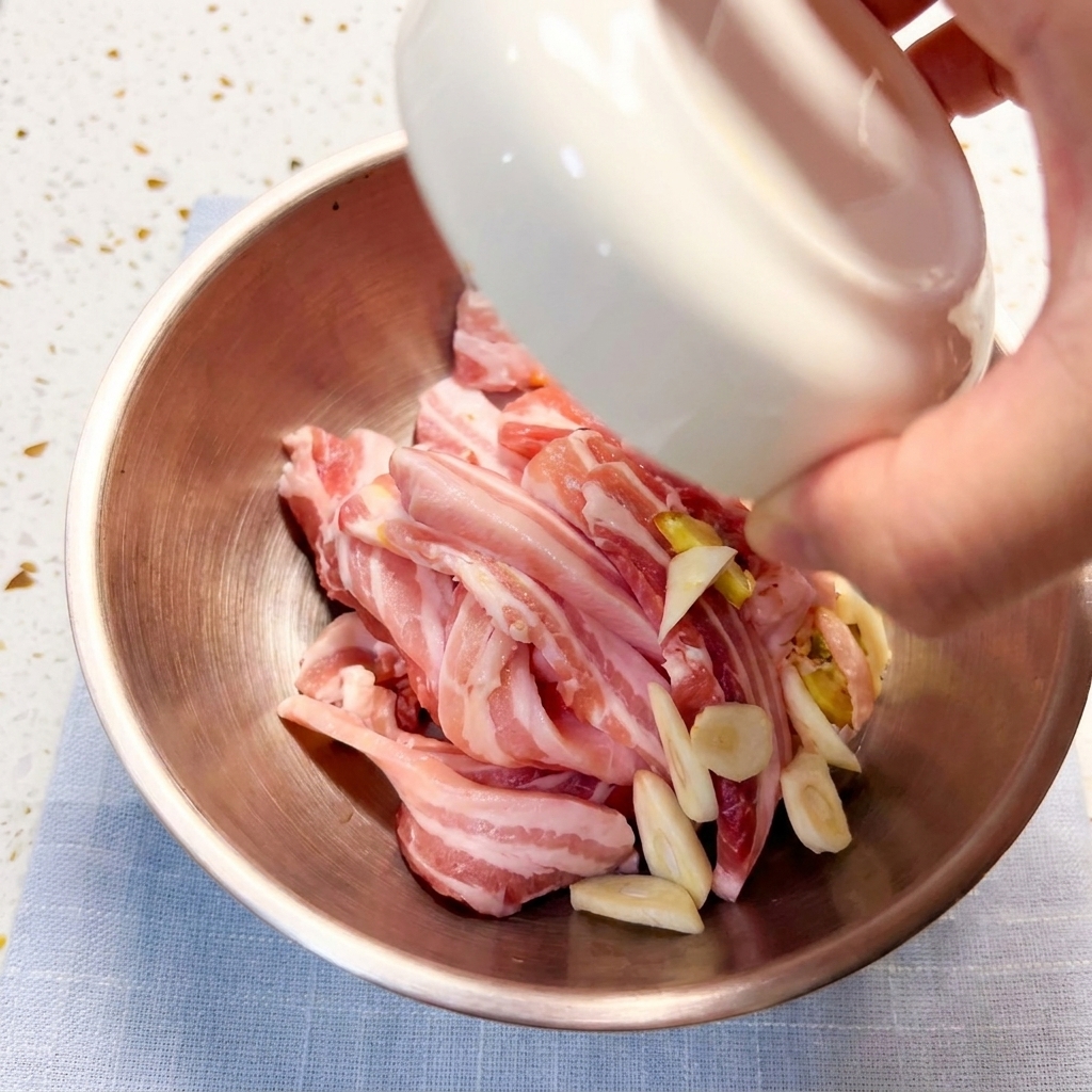 Marinating pork belly slices in a metal bowl with various seasonings and sauce ingredients.