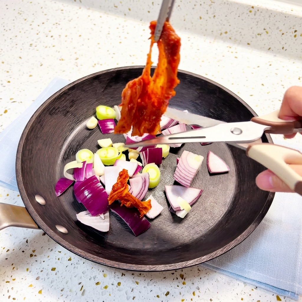 Kimchi being cut with kitchen shears into a pan containing sautéed aromatics.