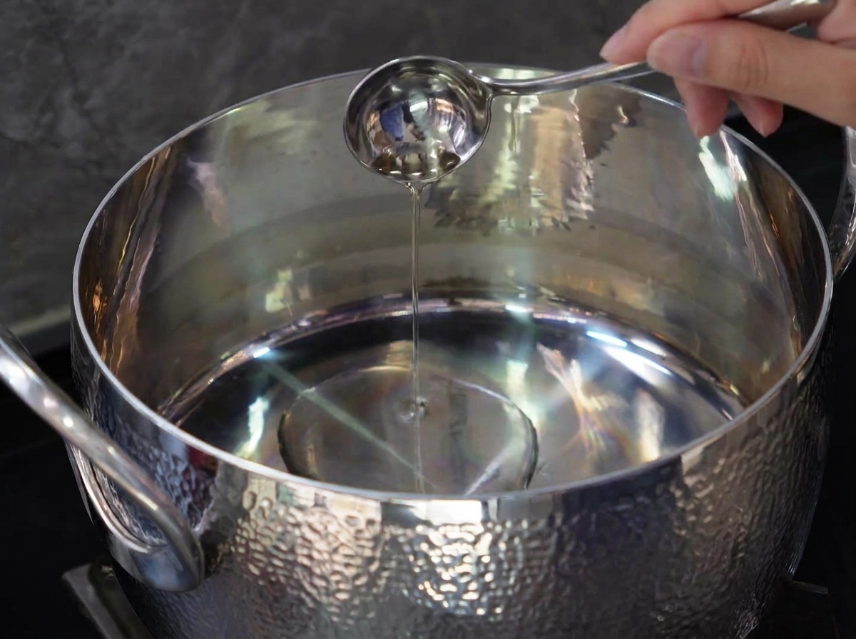 Pork belly pieces frying in a stainless steel pot until golden brown.