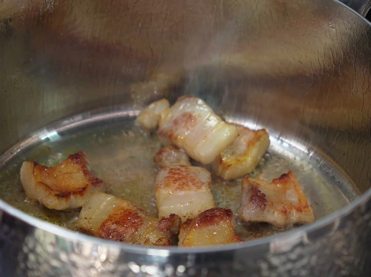 Minced garlic being stirred into the rendered pork fat and browned meat.