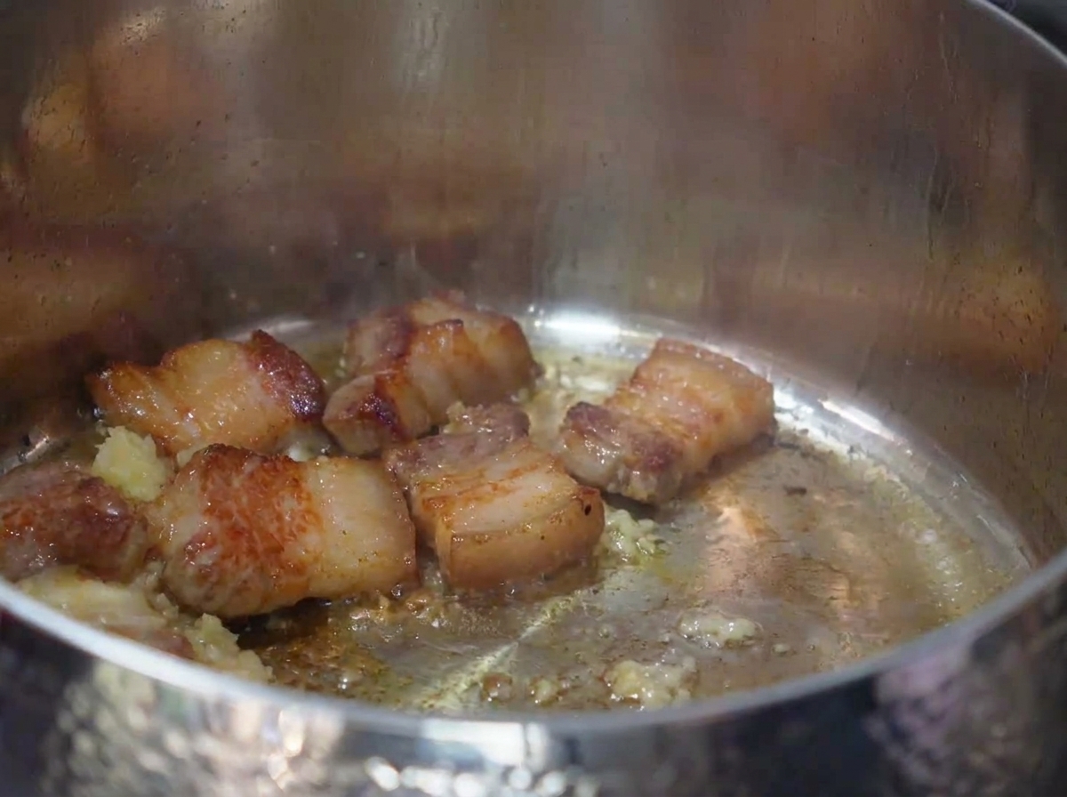 Chopped kimchi being stirred into the pot with the browned pork and garlic.