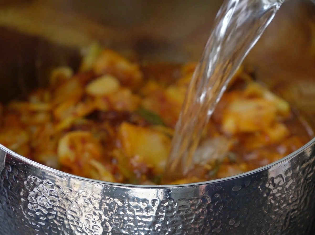 Water being poured into the pot with the kimchi and pork mixture.