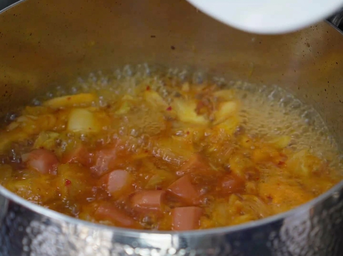 Slices of spam and sausage simmering in the bubbling, seasoned kimchi broth.