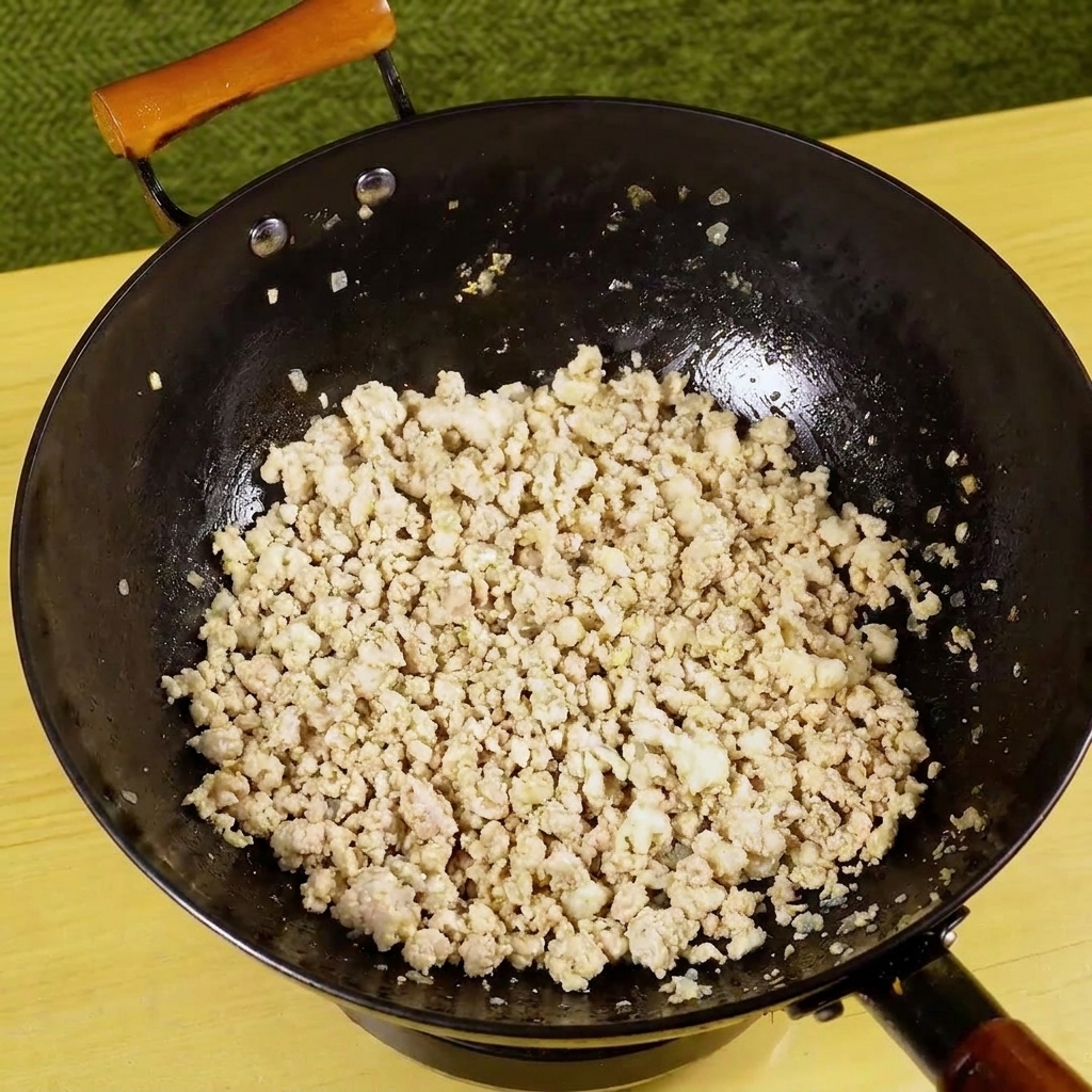 Chopped green chili being added to a pan of cooked, browned minced pork.