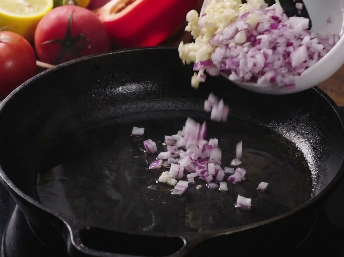 Diced onions and minced garlic being poured into a hot, oiled cast iron skillet.