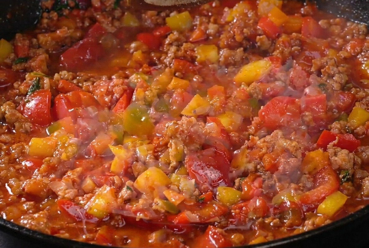 The meat sauce simmering in the pan as it is being seasoned with pepper, showing a rich, thick texture.