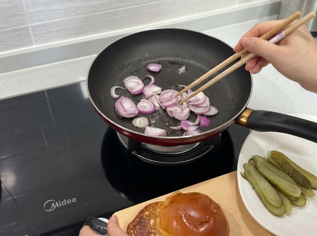Red onion slices being stir-fried in a hot pan using wooden chopsticks.