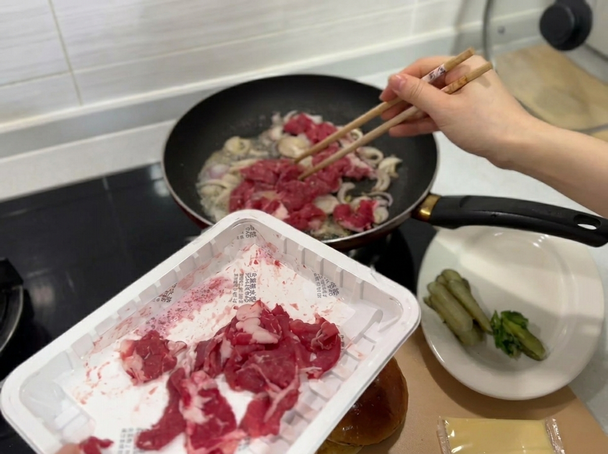 Fresh thin slices of raw beef being added to the pan containing sautéed onions.