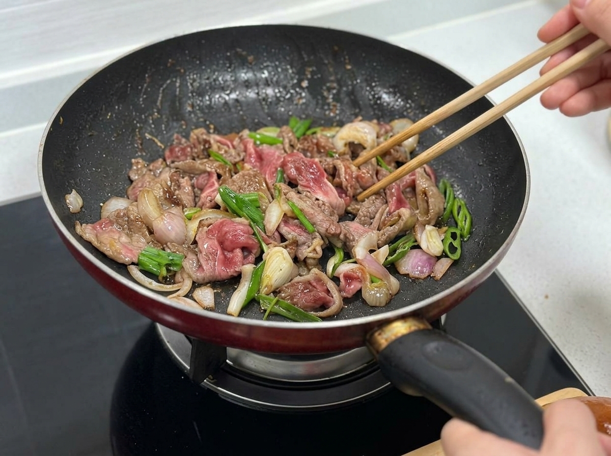 Beef, onions, and green pepper slices being stir-fried together in the pan.