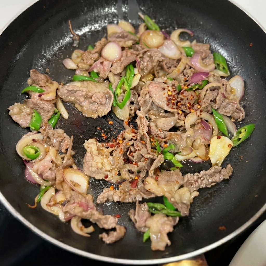 Seasonings being sprinkled over the stir-fried beef, onions, and peppers in the pan.