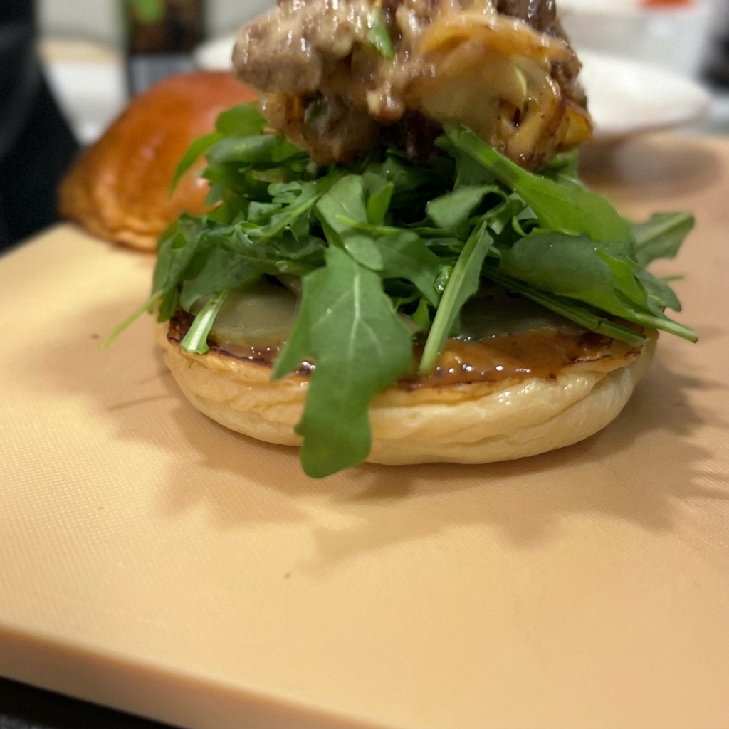 A thick layer of stir-fried beef and red onions topped with melted cheese sitting on a bed of fresh arugula.