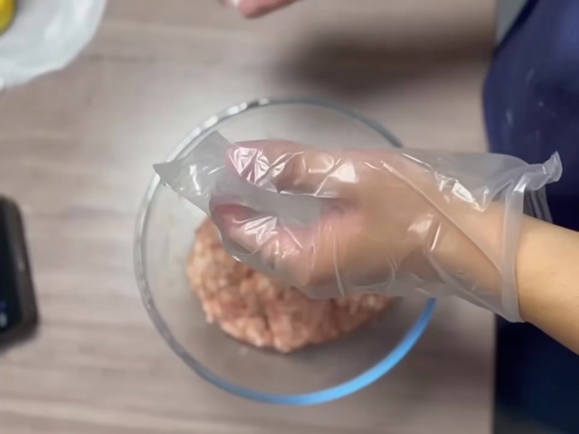 Gloved hands shaping a portion of meat into a firm, smooth ball.