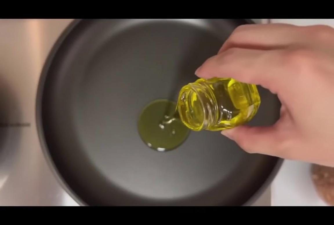Four raw burger patties sitting in a hot frying pan with olive oil and whole garlic cloves.