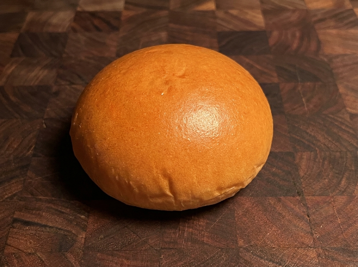 A golden-brown toasted burger bun resting on a wooden surface.