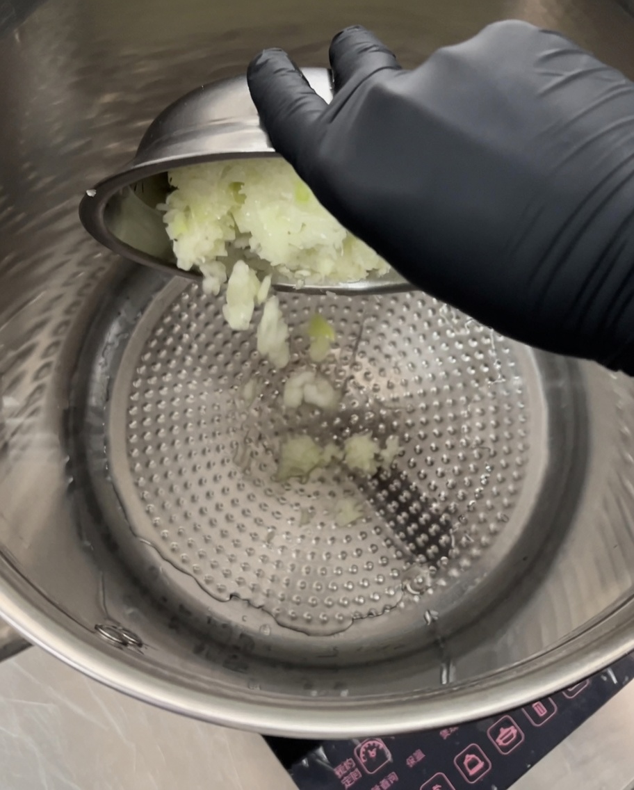 Finely chopped onions being stirred in a large stainless steel pot over medium heat.