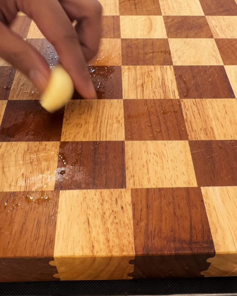 Garlic cloves being finely minced on a wooden cutting board with a large knife.
