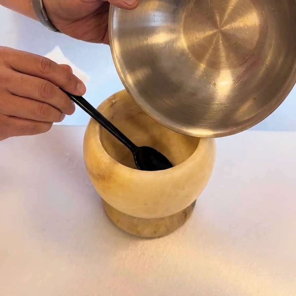A close-up of a stone mortar and pestle grinding fresh chilies and minced garlic into a textured paste.