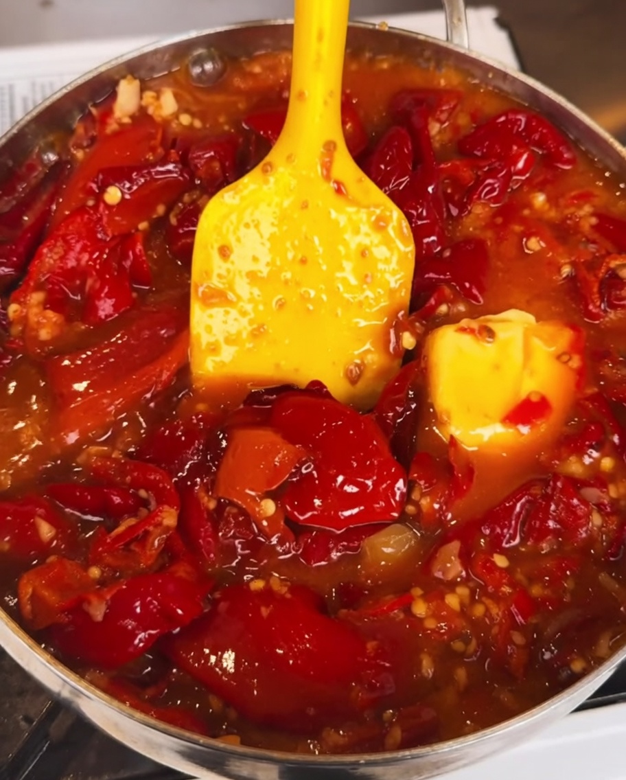 The chili sauce simmering in a pan as a thick, dark sauce is stirred in, creating a rich and glossy finish.