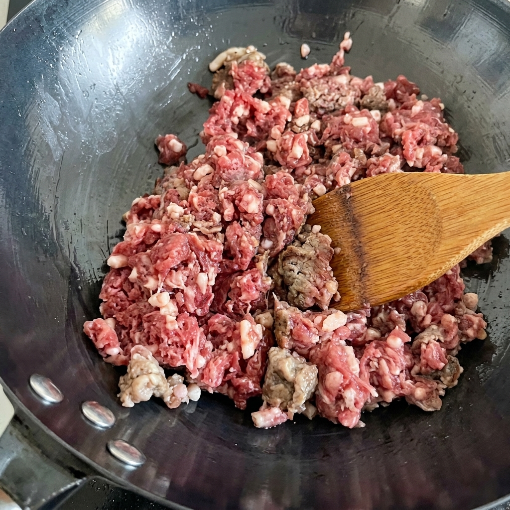 Fresh minced beef being stir-fried in a hot wok, changing color from red to brown.