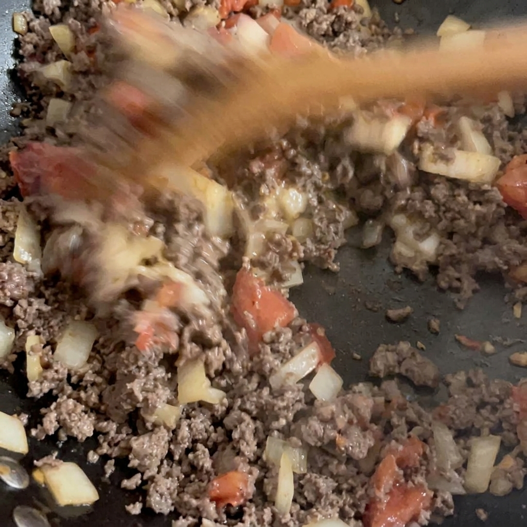Browned ground beef and sautéed diced vegetables being mixed together in a wok.