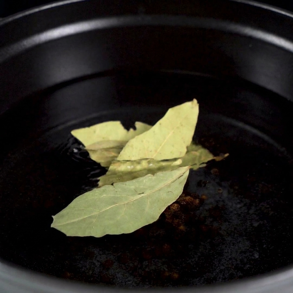 A raw lobster being placed into a pot of aromatic boiling water with visible peppercorns and bay leaves.
