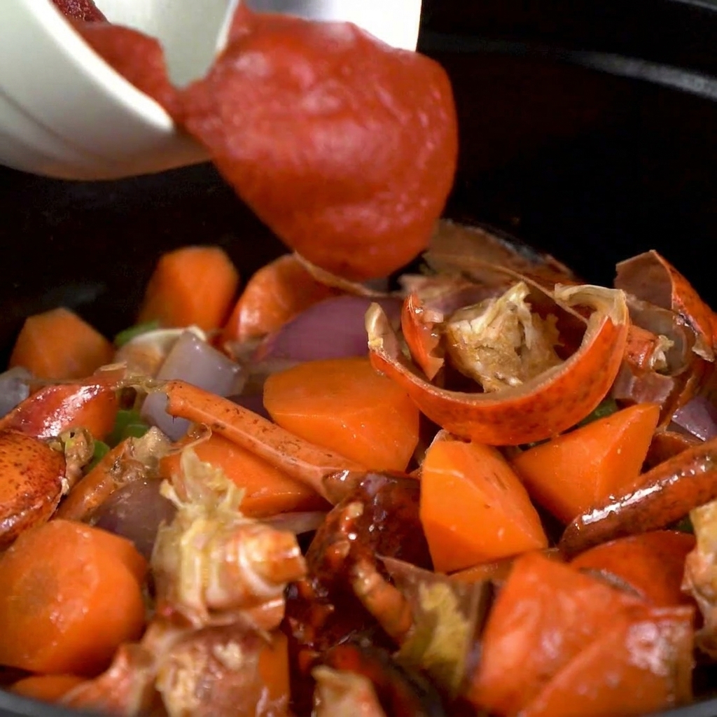 Tomato paste being stirred into the pot of vegetables and lobster shells.