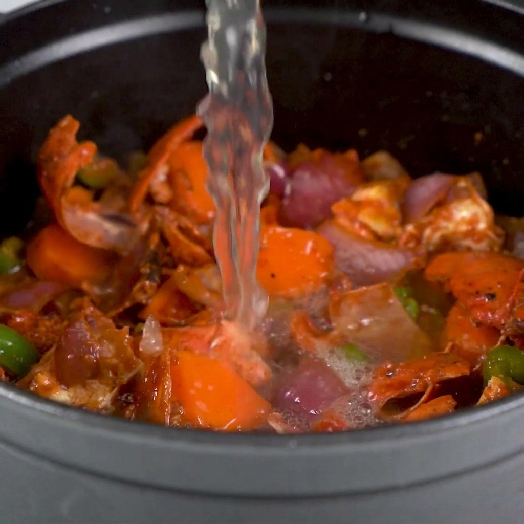 Stock being poured over the lobster shells and sautéed vegetables in a large pot.