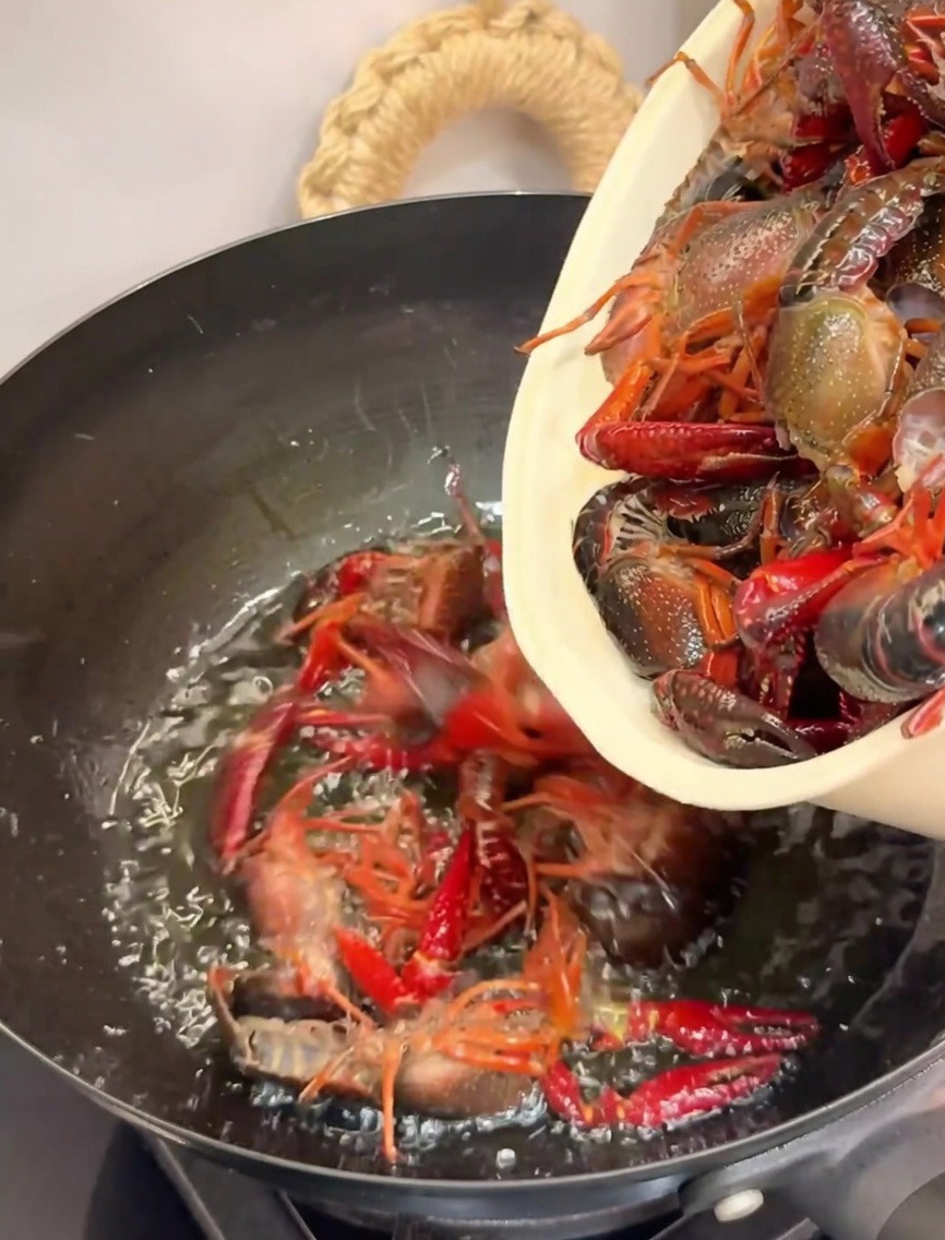 Crayfish being added to a hot wok filled with oil for frying.