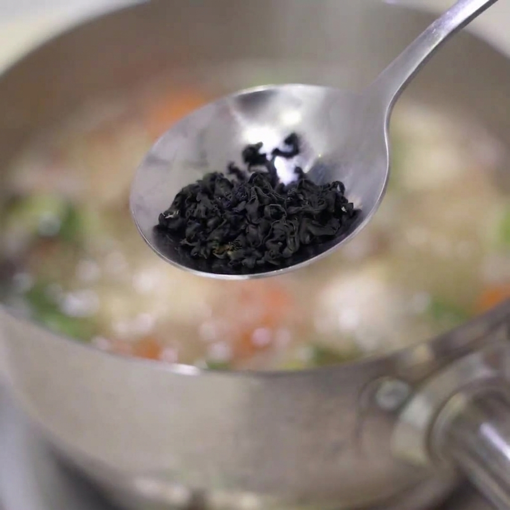 Dried wakame seaweed being added into a pot of simmering soup with carrots and other ingredients.