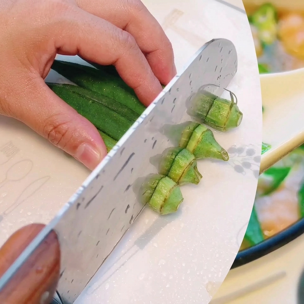 Fresh green okra being carefully sliced into smaller, uniform sections on a cutting board.