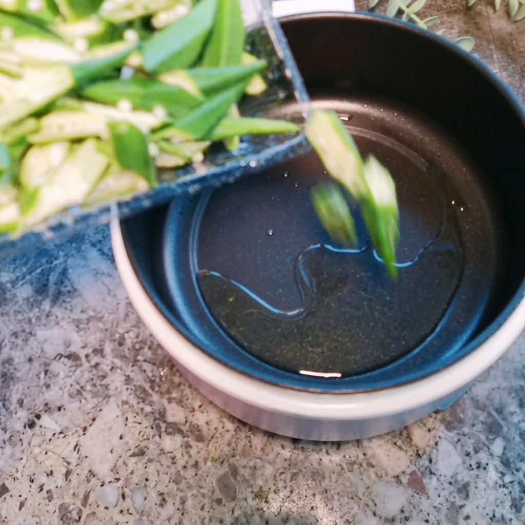 Sliced okra pieces being stir-fried in a hot pot with a little oil.