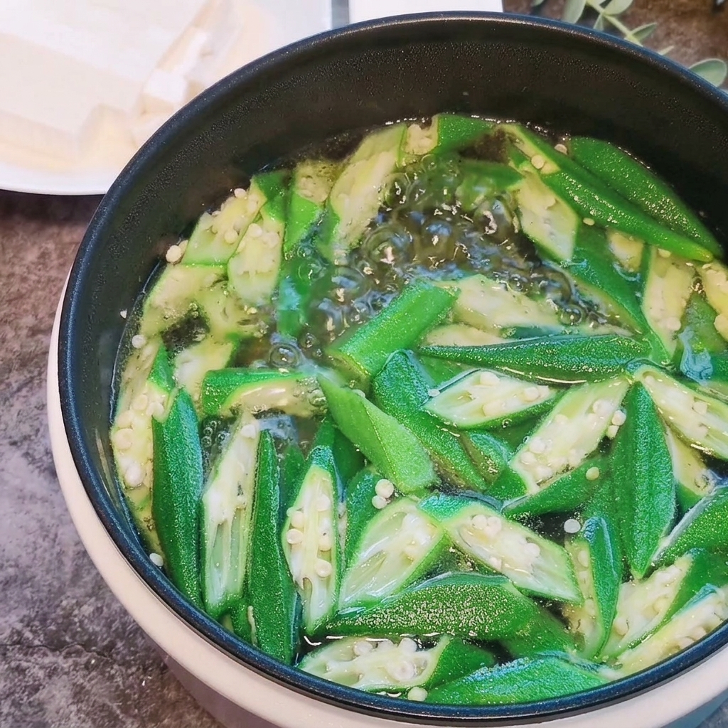 Soft tofu cubes being added to a boiling pot of okra and water.