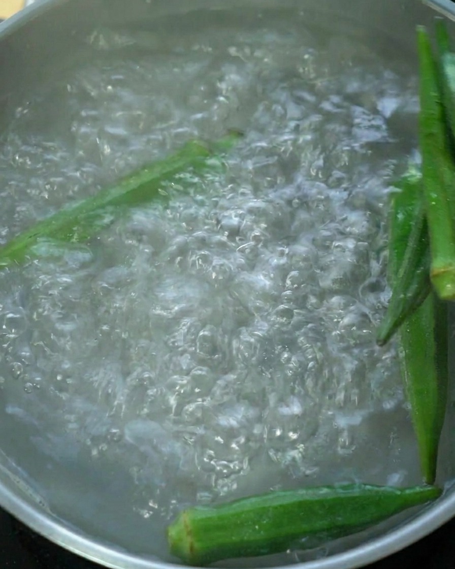 Fresh green okra pods boiling in a pot of water.