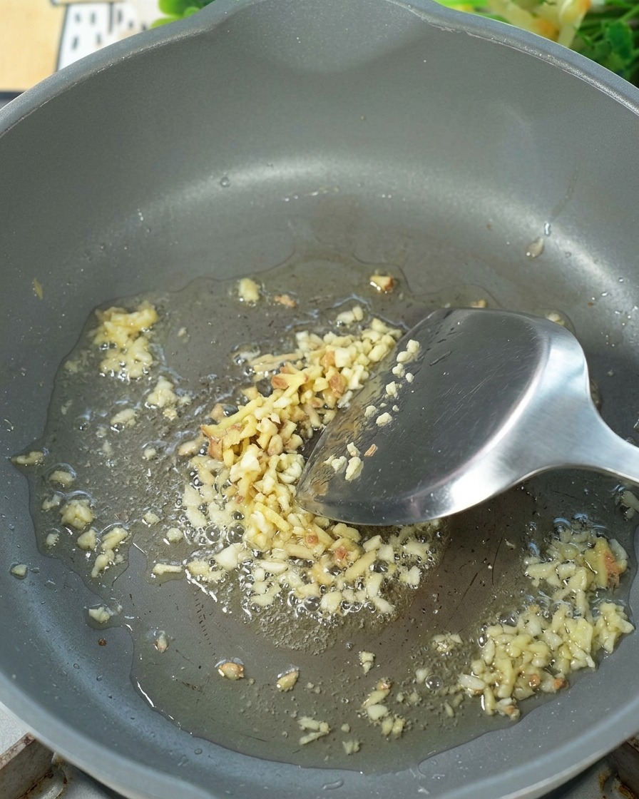 Minced ginger being sautéed in hot oil in a frying pan.