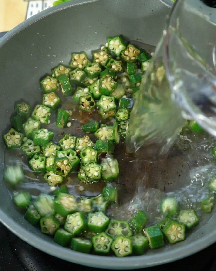 Water being poured into a pan containing stir-fried okra.