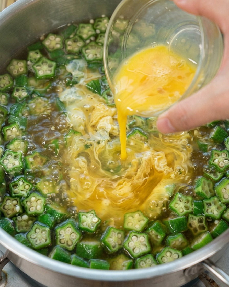 Beaten egg being poured into boiling okra soup to create ribbons.