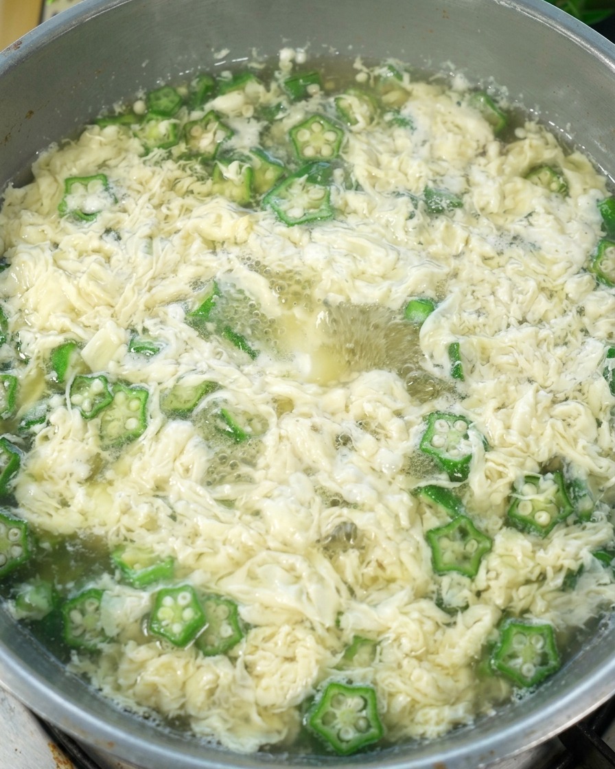 Okra Egg Drop Soup in the pot with salt being stirred in, ready for serving.