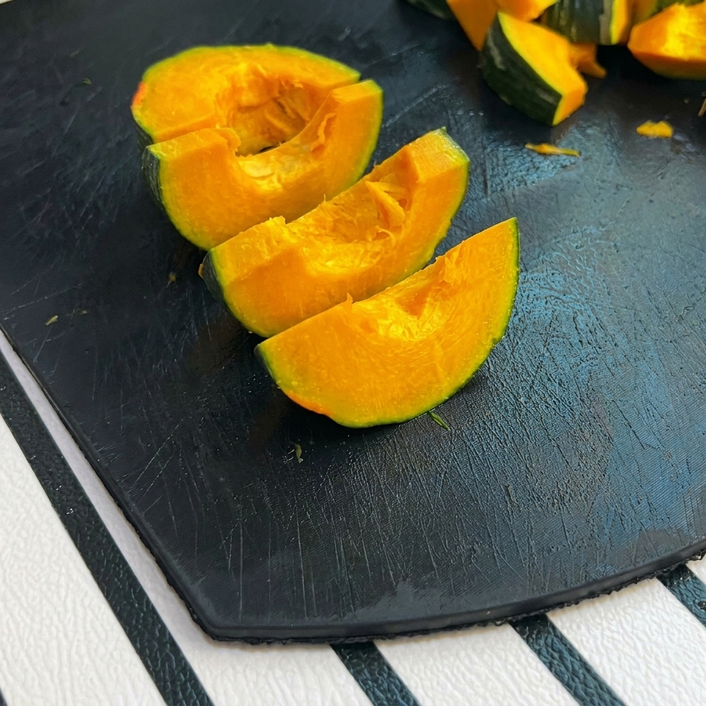 Small wedges of green-skinned pumpkin sitting on a black cutting board.