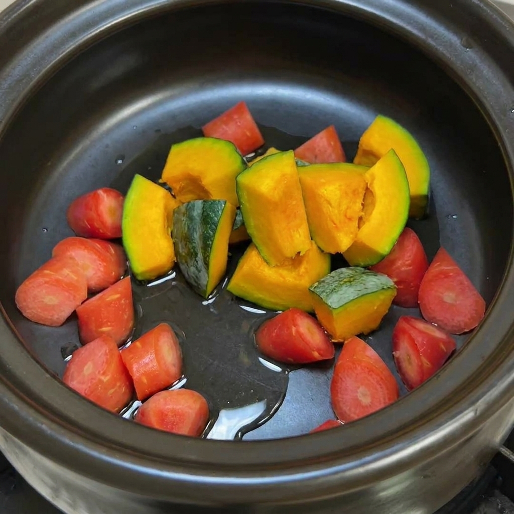 A black clay pot containing chunks of green-skinned pumpkin and bright orange carrots glistening with oil before being stir-fried.