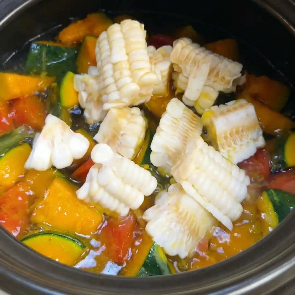 Freshly cut corn segments being added into a pot of bubbling vegetable soup.