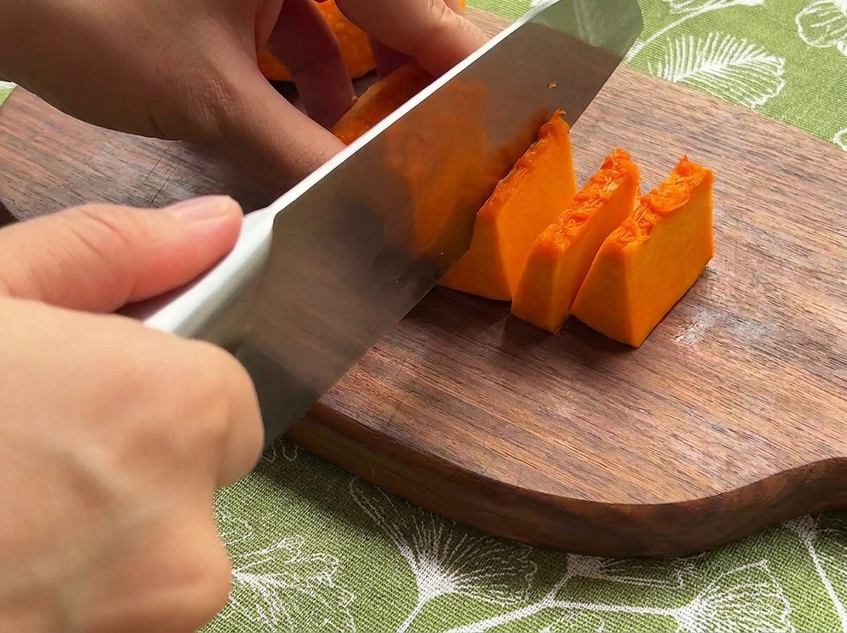 Fresh pumpkin, onion, and carrots being sliced into small, even pieces on a wooden board.