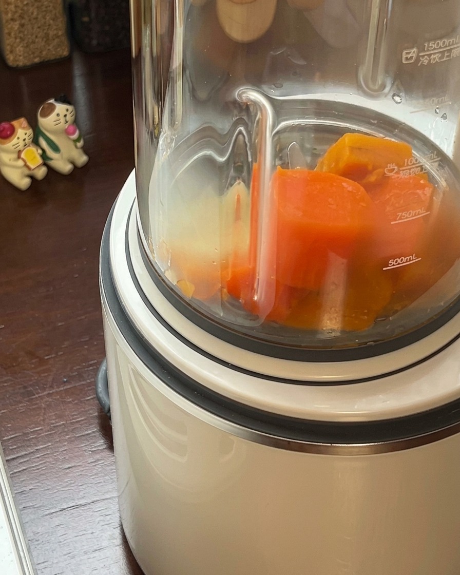 Cooked pumpkin and carrot mixture being poured into a high-speed blender jar.