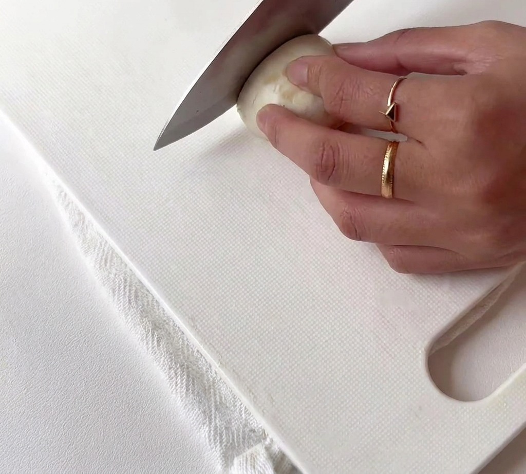 Garlic cloves being cut into halves on a white surface.