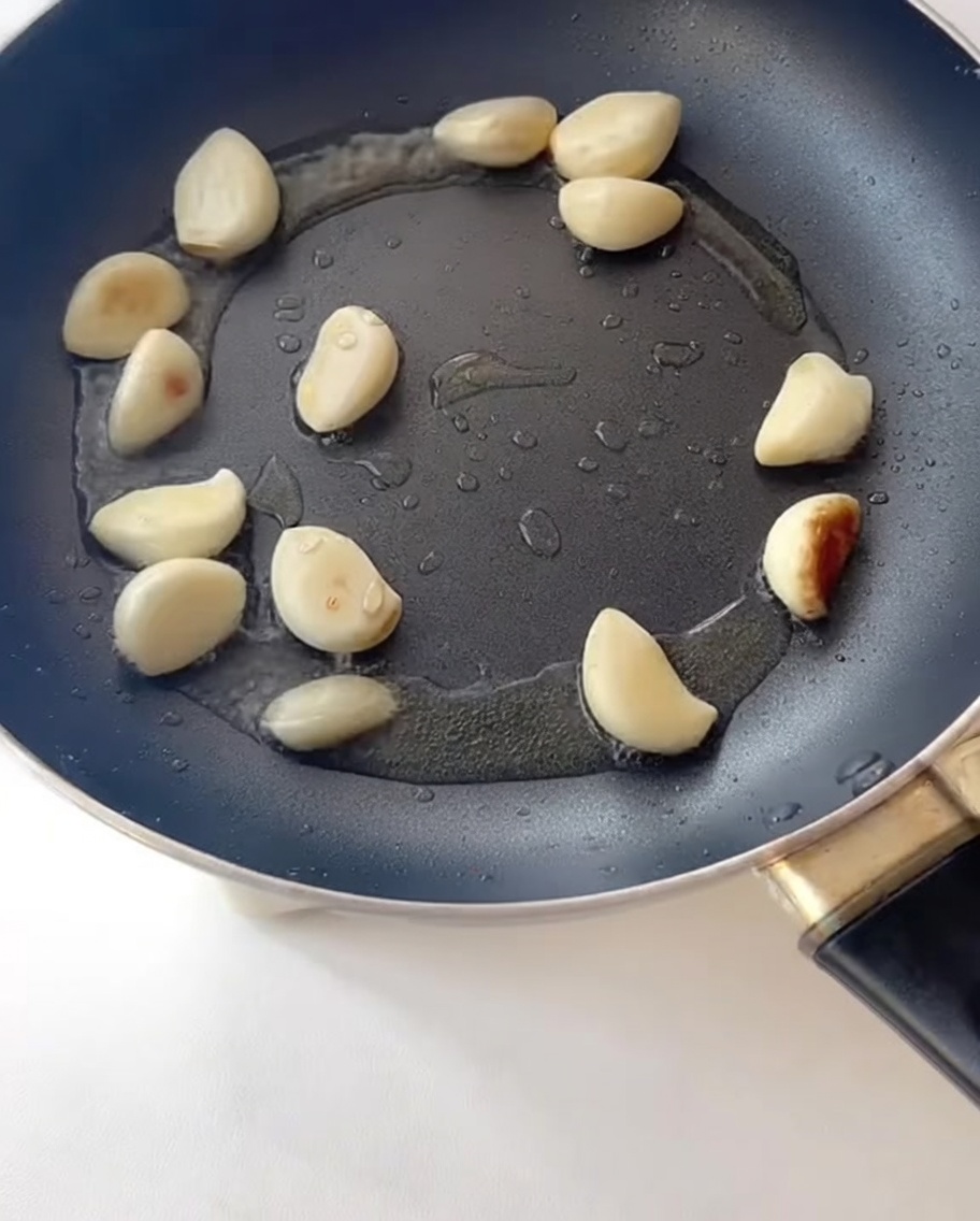 Slices of bacon frying in a pan alongside sautéed garlic.